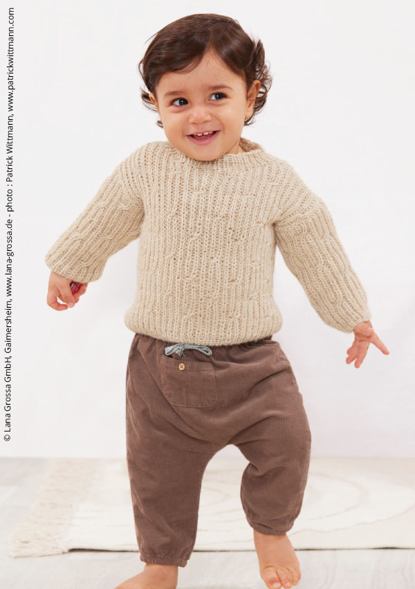 Jeune enfant marchant pieds nus, vêtu d'un pull en grosse maille beige côtelé et d'un pantalon en velours côtelé marron à taille élastique, sur un tapis clair.